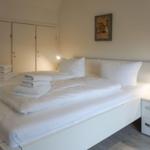Schlafzimmer mit weißem Bett, Nachttisch und Kleiderschrank.