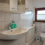Badezimmer mit Waschbecken, Spiegel, Toilette und Fenster.