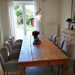 Esszimmer mit massivem Holztisch und Stühlen, Glasfront zum Garten, Hängelampe und Sideboard.