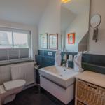 Bathroom with sink, toilet, and window. Wall mirror and basket are present.