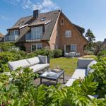 House with garden, terrace, and seating. Rose bushes and green plants surround the outdoor area.