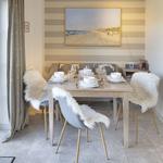 Dining table with four chairs, white fur covers, and beach painting on the wall.