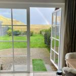 Through the glass door, one sees a paved courtyard with lawn and a rainbow over the dunes.
