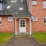 Red brick building with white windows and entrance door. Lawn and stone path in front.