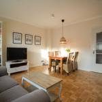 Living and dining area with sofa, TV, table and chairs on parquet floor.