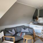 Wohnbereich mit Sofa, Stühlen und Küchenzeile unter Dachschrägen.
