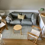 Ein Wohnbereich mit grauem Sofa, zwei Stühlen und einem runden Tisch.