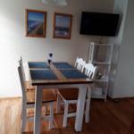Dining area with table, chairs, and wall pictures. TV mounted on the wall.