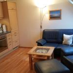 Living area with kitchen, sofa, and armchairs under sloped ceiling.