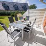 Terrasse mit Tisch und Stühlen, Garten und Haus im Hintergrund.