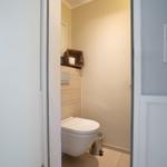 Behind the door, a toilet with a basket and trash can is visible.
