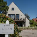Modern villa with balcony and sign NIILÖN. Surrounded by trees and shrubs.