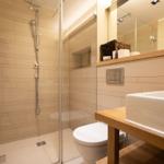 Shower with glass enclosure, sink with wooden vanity, and toilet.