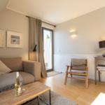 Living room with sofa, chair, and table. Window with curtains. Wall art and lighting.