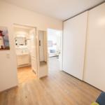 Hallway with bedroom, bathroom, and living room. Wall picture shows a lighthouse.