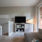 Wohnzimmer mit Sofa, Fernseher und Bücherregal. Fensterblick auf Außenbereich.