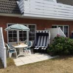 Terrasse mit Tisch, Stühlen und Sonnenschirm neben Strandkörben.
