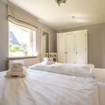 Schlafzimmer mit weißem Bett, Kleiderregal und Fensterblick