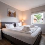 Schlafzimmer mit Bett, Nachttisch und Fenster. Auf dem Bett liegen gefaltete Handtücher.