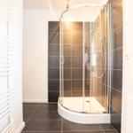 Dusche mit Glaswand und dunklen Fliesen. Heizung links. Bodenfliesen schwarz.