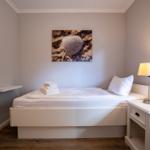 Schlafzimmer mit weißem Bett, Nachttisch und Wandbild mit Muschel.