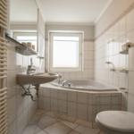 Badezimmer mit Badewanne, Waschbecken und Toilette. Fliesenwand und Fenster sichtbar.