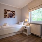 Ein Schlafzimmer mit Bett, Nachttisch und Fenster mit Blick auf Bäume.