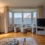 Wohnzimmer mit Holzboden, TV, Fenster und Tischen.