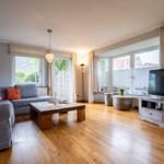 Wohnzimmer mit Sofa, Holztisch und TV. Holzfußboden und große Fenster.