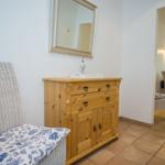 Holzschrank mit Spiegel, weiße Rattanbank mit blau-weißem Kissen.