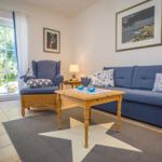 Wohnzimmer mit blauem Sofa, Holztisch und Blick auf den Garten.