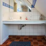 Badezimmer mit Waschbecken, Spiegel und Terrakottboden