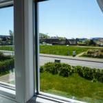 Durch das Fenster blickt man auf eine grüne Wiese und Straßen im Dorf.