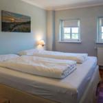 Schlafzimmer mit Doppelbett, zwei Fenstern und Wandbild.