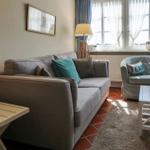 Wohnzimmer mit Sofa, Sessel und Tisch. Fenster mit Vorhängen. Teppich und Bodenfliesen.