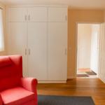 A room with a red armchair, white wardrobes, and wooden furniture.