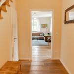Hallway with wooden staircase and view into living room with sofa and window.