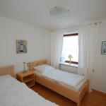 Two beds, window with curtains, nightstand, and pictures on the walls.