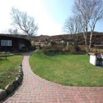 House with garden, stone path, and grill. Background: hills with trees.