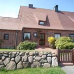 Red tile roof, brick house with entrance door and stone wall. Wooden gate with number 62.