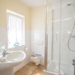 Bathroom with shower, sink, and toilet. Window with white curtains.