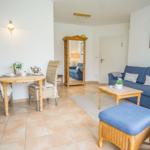 Living and dining area with blue sofa, wooden table and chairs, mirror and teapot.