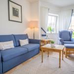 Blue sofa with cushions, armchair and table in living room with garden view.