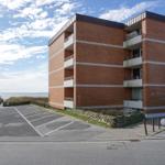 Rotes Backsteinhaus mit Balkonen und Parkplatz neben dem Meer.