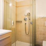 Bad mit Dusche, Waschbecken und Toilette. Fliesenwand und Spiegel sind sichtbar.