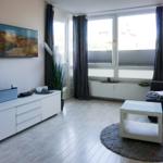 Wohnzimmer mit Sofa, Fernseher und großen Fenstern.