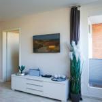 Wohnzimmer mit Fernseher, weiße Kommode und Blick auf Balkon