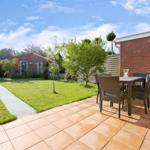 Terrace with table, chairs, and beach chair. Lawn and garden path in background.