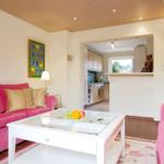 Living area with pink sofas, glass table, and view into the kitchen.