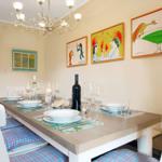 Dining table with white chairs and plaid cushions. Wall art and chandelier.